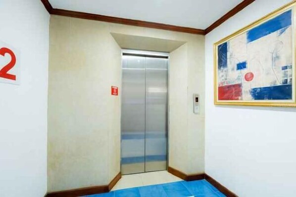 A narrow hallway with a blue mat at the entrance, an elevator, and a large abstract painting on the wall. - Lamai Hotel (Phuket)