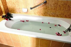 A bathtub with rose petals, a handrail, and a small plant. - Lamai Hotel (Phuket)