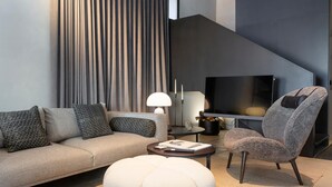 Una sala de estar moderna con sofá, reposapiés y sillón, una mesa de centro y televisor.