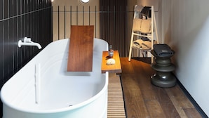 Un baño moderno con una bañera independiente, un estante de madera, una mesita con una botella y un cuenco, un perchero y una silla de masaje.