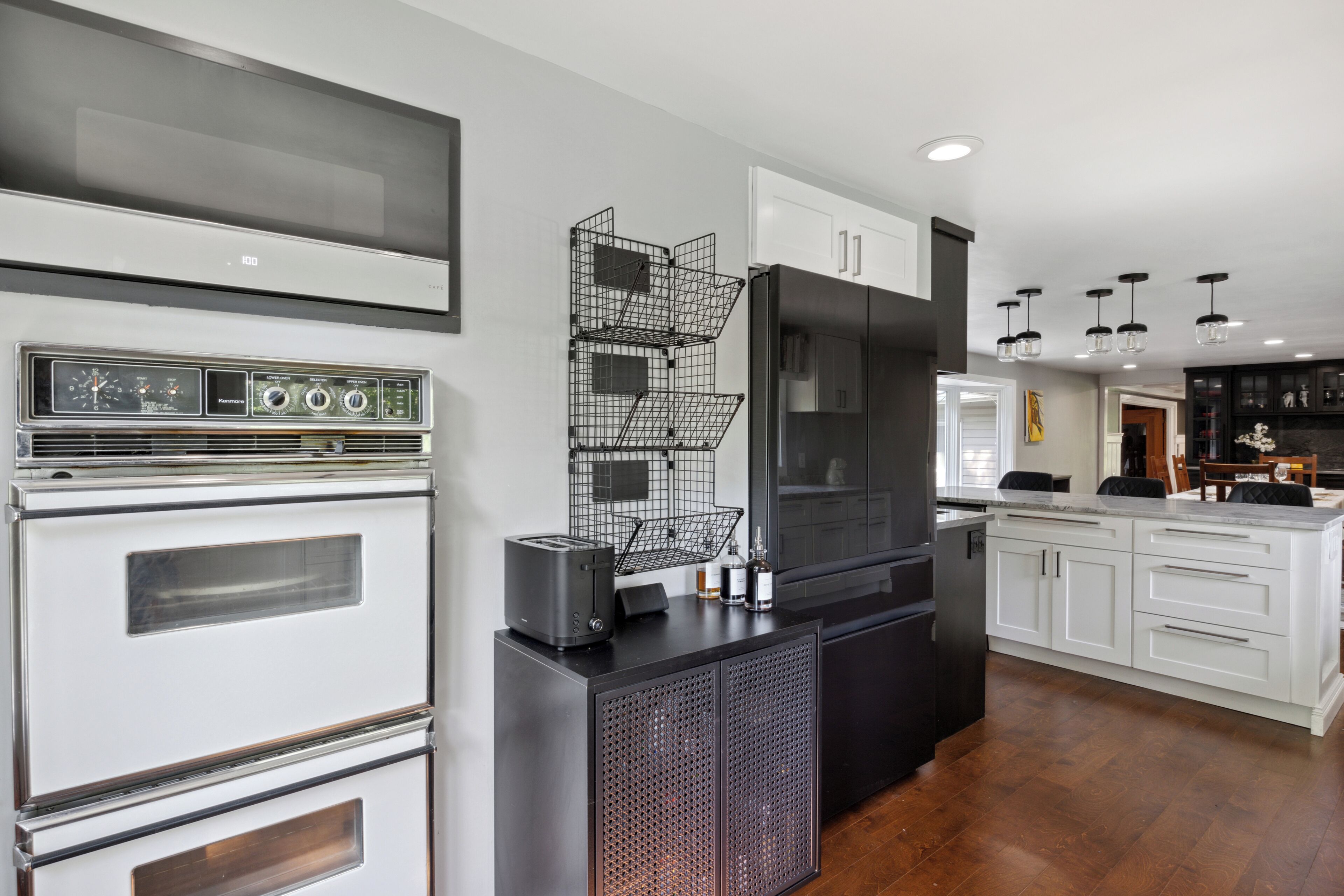 Una cocina moderna con horno empotrado, refrigerador negro, armarios blancos y encimera negra.