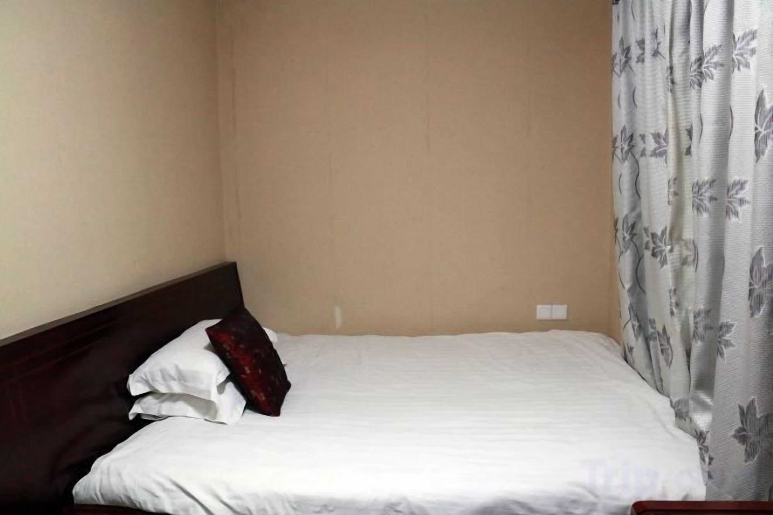 A bed with a headboard, a white bedspread, and a floral-patterned curtain.
