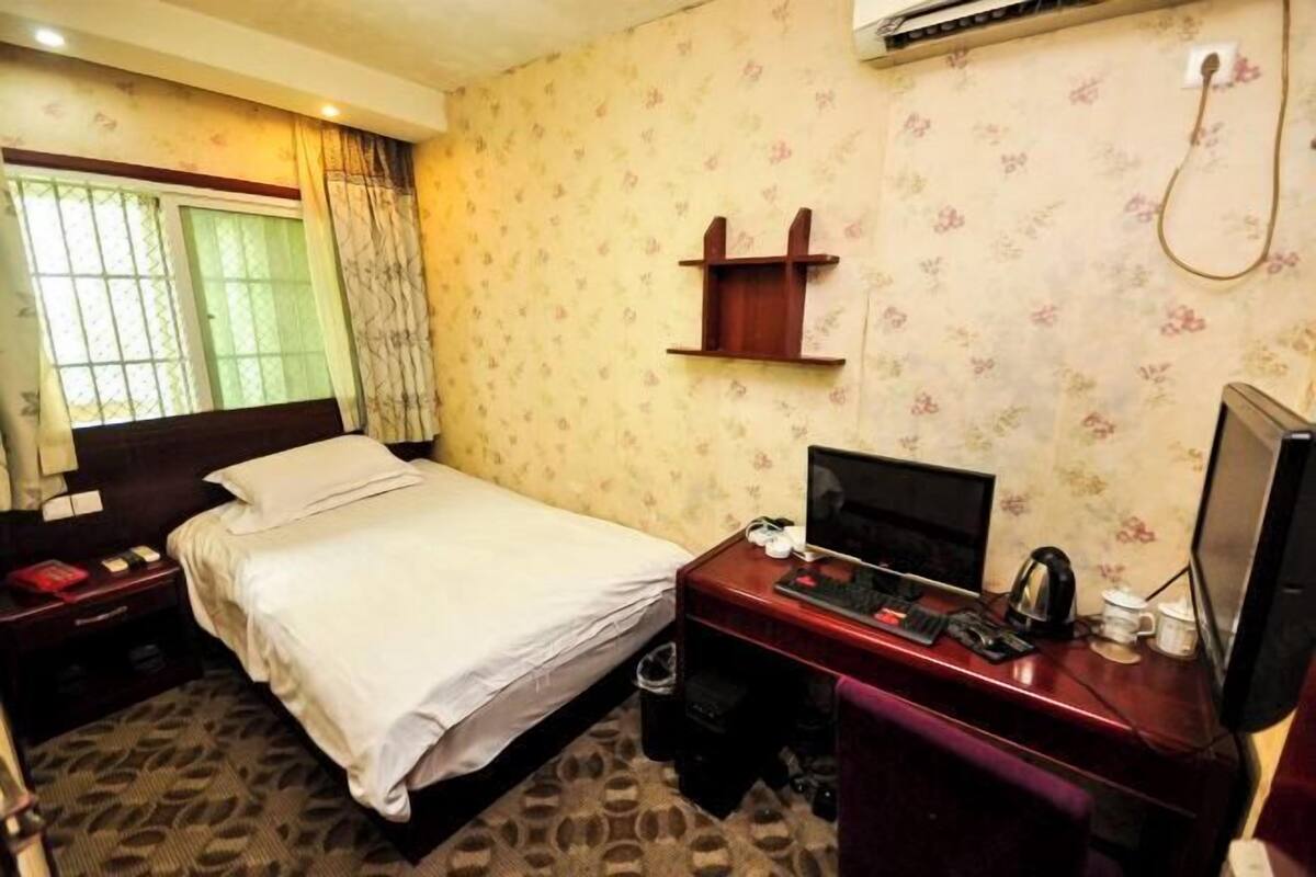 Ein Hotelzimmer mit Bett, Schreibtisch, Computer, Fernseher und einer kleinen Ablagefläche.