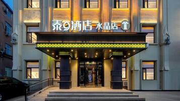 A hotel entrance with illuminated signage, a covered entrance, and a car parked in front.