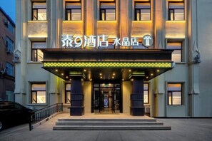 A hotel entrance with a sign in a foreign language, a covered entrance area, and a car parked in front. - Thai 9 Business Hotel Crystal Shop (Daqing)