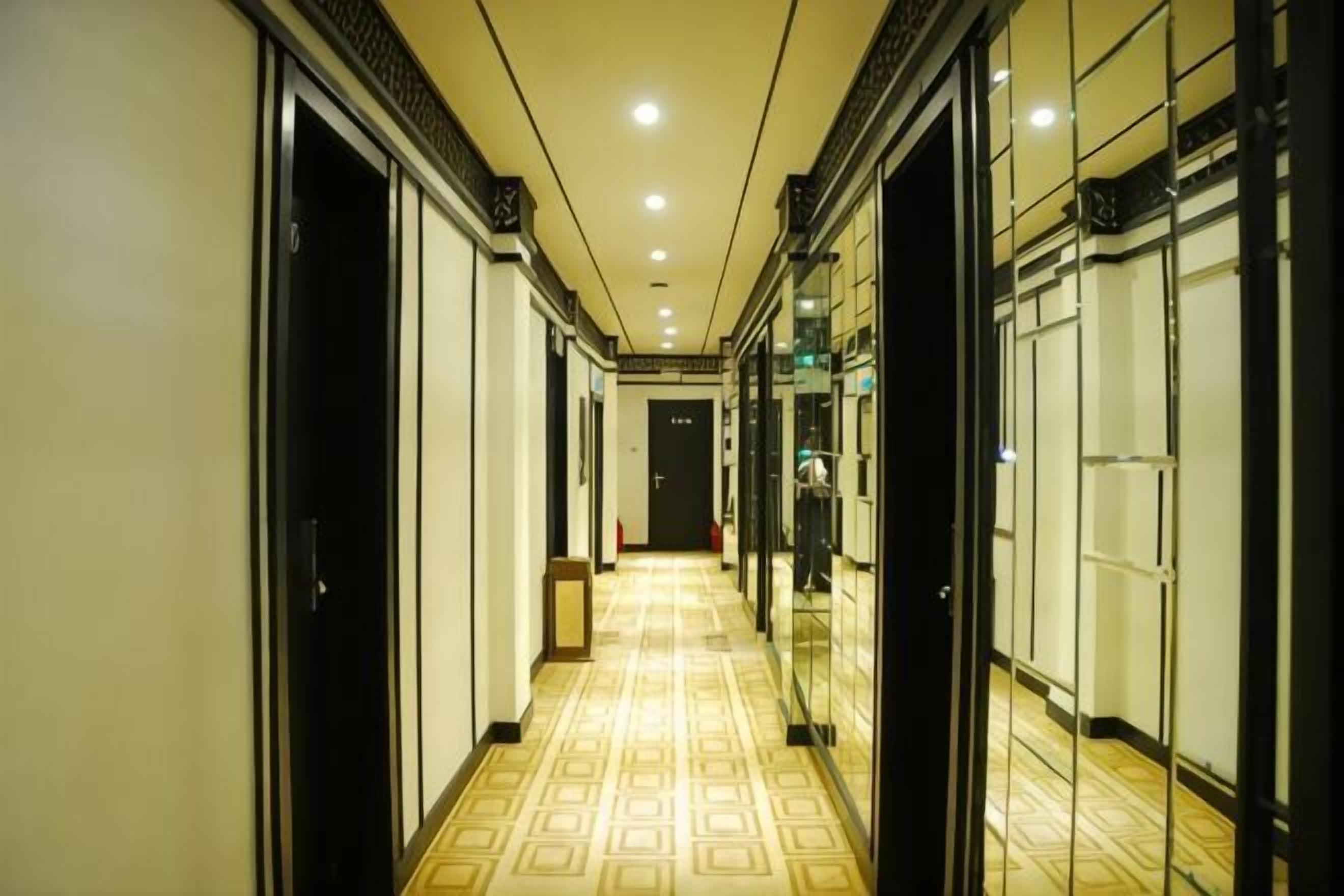 Un couloir d’hôtel avec des portes des deux côtés, un sol à motifs et un éclairage encastré.