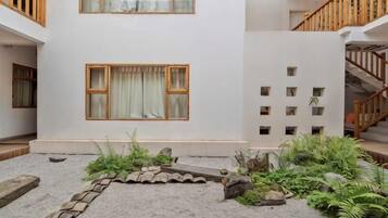 A building with a white exterior, a staircase, and a small garden area with plants and a stone pathway.