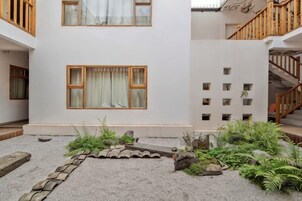 Um edifício com fachada branca, uma escadaria e um pequeno jardim com plantas e um caminho de pedra.