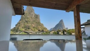 A view from a balcony with a wooden ceiling, overlooking a mountainous landscape with two prominent peaks and several houses in the background. - Shifang Chuanshe Boutique Inn (Zhaoping)