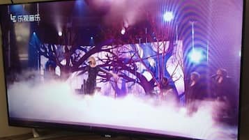 A television displaying a scene with a person in a dark outfit, a tree-like structure, and a smoky background.