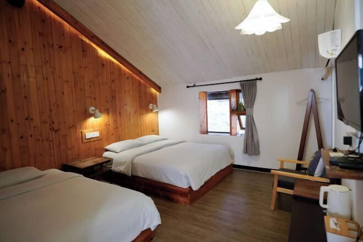 Una habitación con dos camas, paredes de madera, una ventana con cortinas, un escritorio con silla y un televisor de pared.