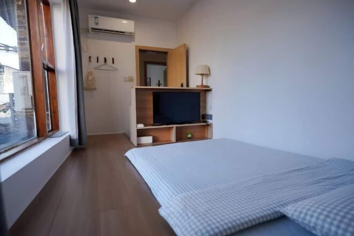 Un dormitorio con cama, televisor, espejo y ventana.