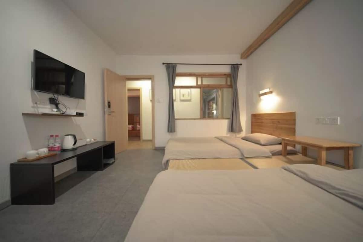 Habitación de hotel con televisión, escritorio con tetera, dos camas, espejo y ventana con cortinas.