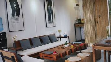 A modern living room with a sofa, coffee table, and chairs. There are framed artworks on the wall and a small table with decorative items.
