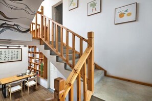 A staircase with wooden railings leading to a landing, a dining area with a table and chairs, and a bookshelf filled with books. - Shifang Chuanshe Boutique Inn (Zhaoping)