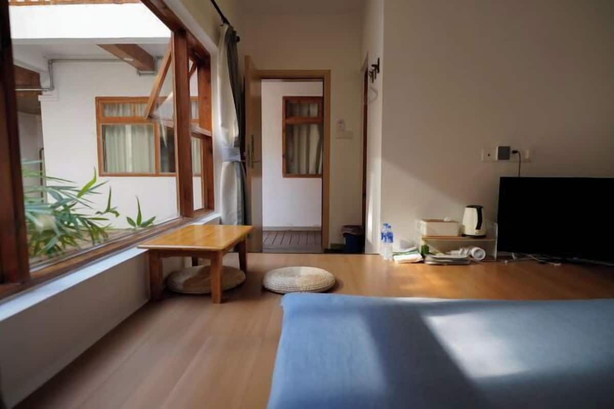 Una habitación con cama, una mesita, una ventana con vistas a zonas verdes, una puerta y un televisor.