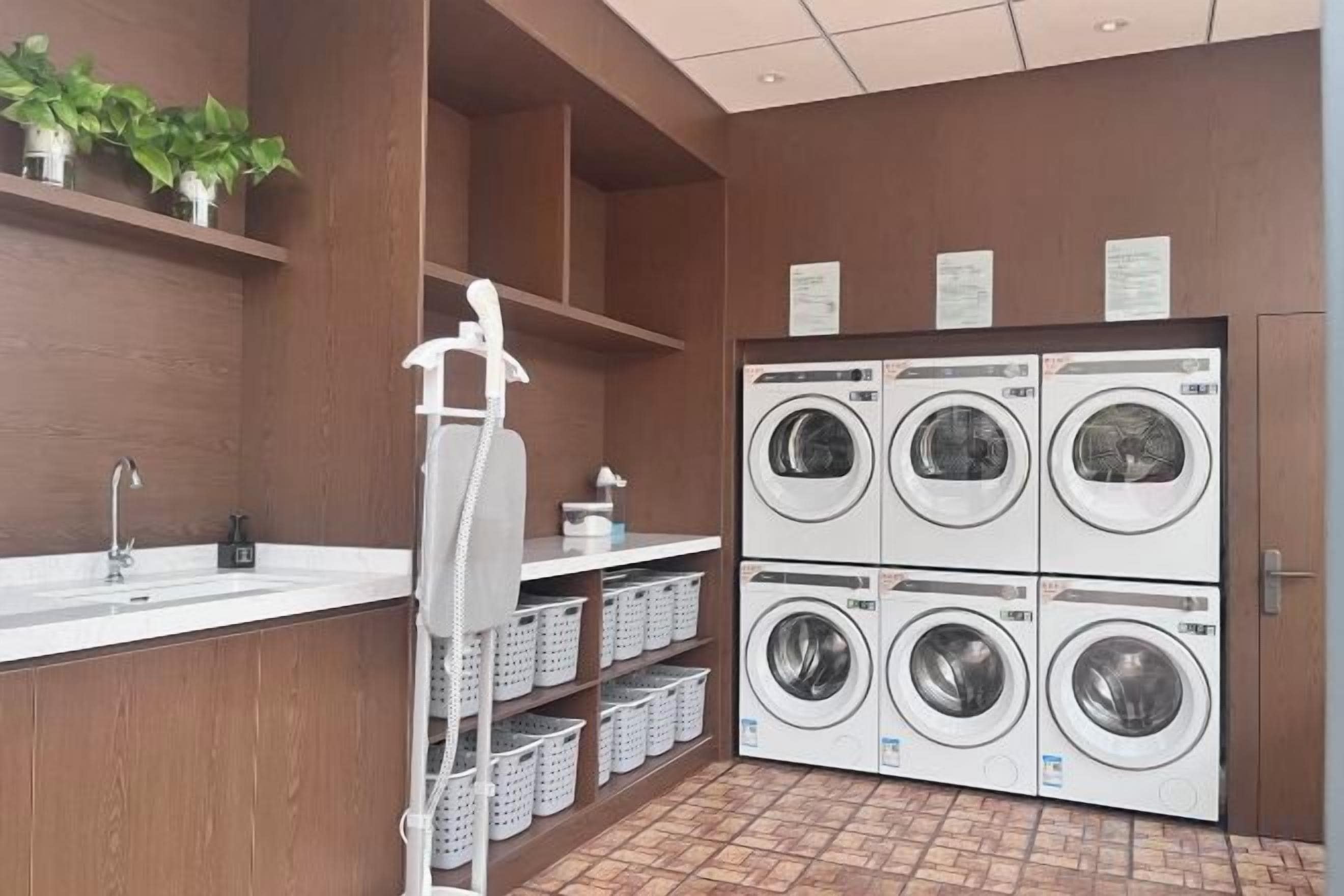 A laundry area with four washing machines, a sink, and shelves with plants.