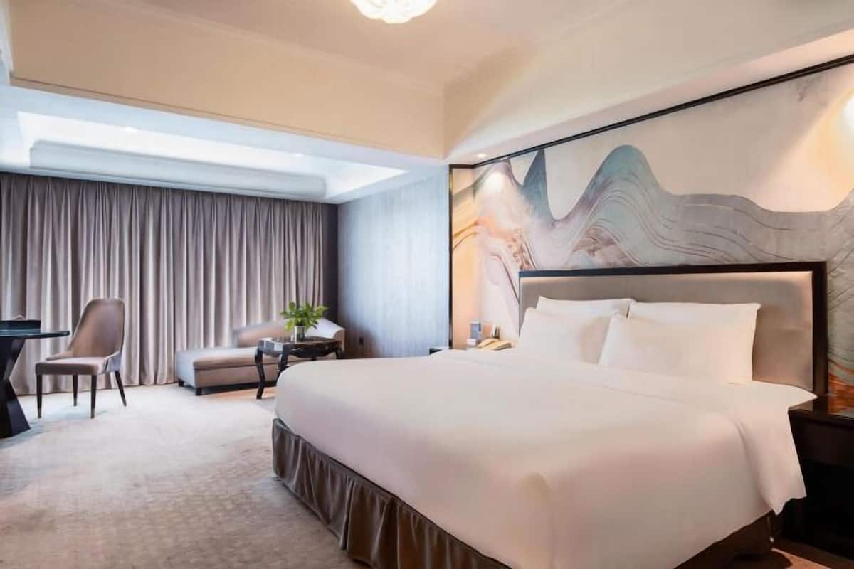 A hotel room with a large bed, a desk, a chair, and a view of the sky through a skylight.