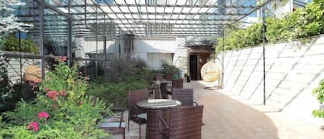 Un patio al aire libre con mobiliario de mimbre, techo de cristal y un sendero de ladrillo.