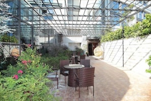 Un patio al aire libre con mobiliario de mimbre, techo de cristal y un sendero de ladrillo.