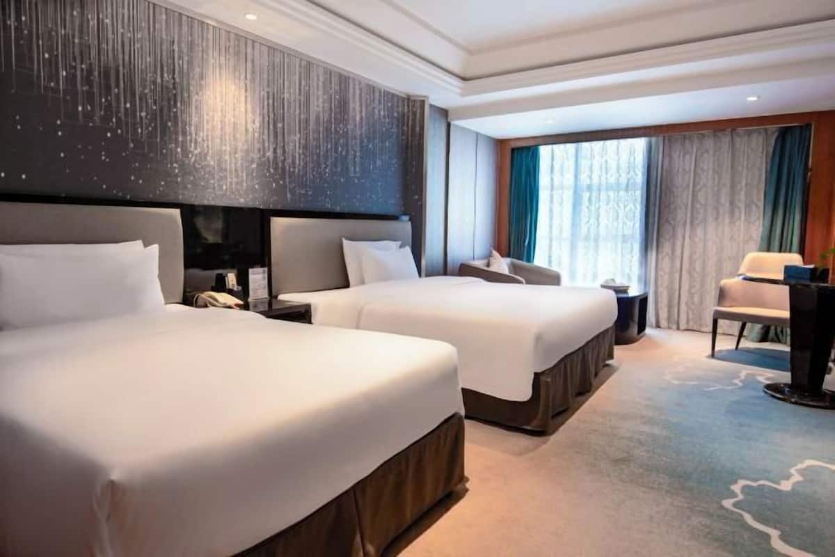 A hotel room with two beds, a desk, a chair, and a large window with curtains.