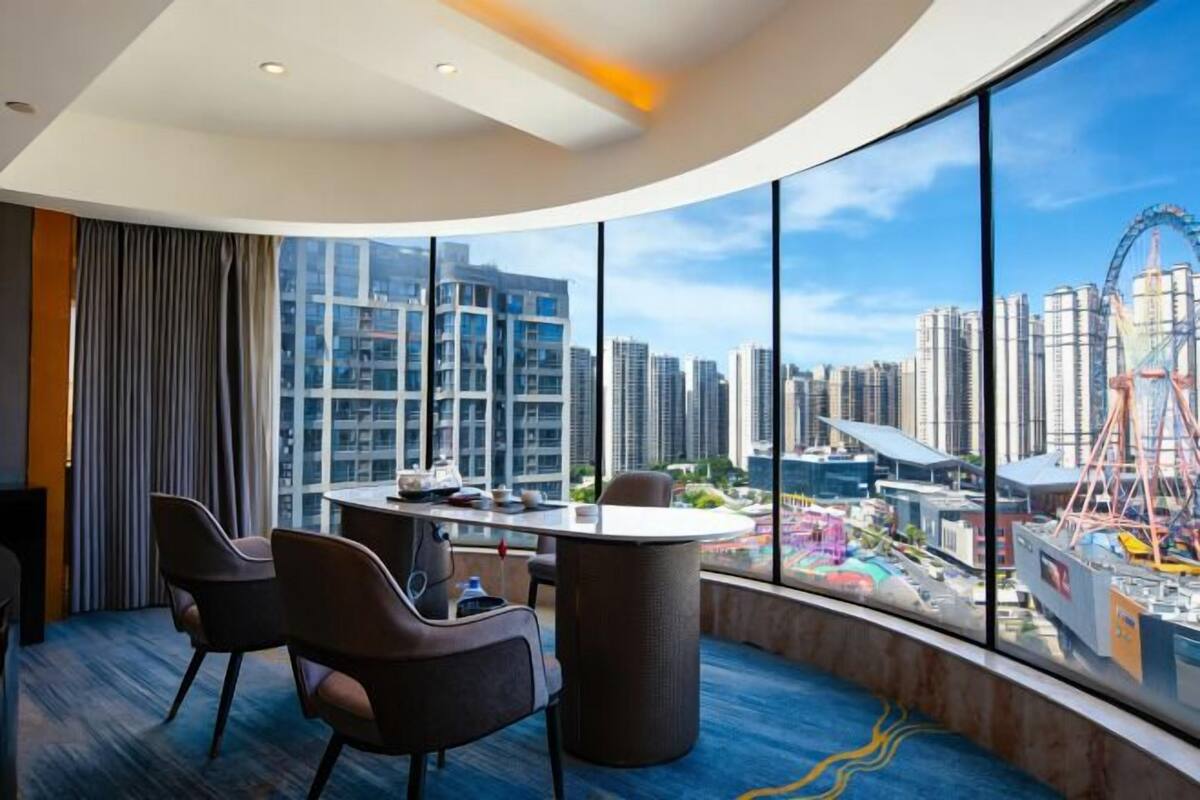 A modern hotel room with a curved ceiling, large panoramic windows, a round table, and several chairs.