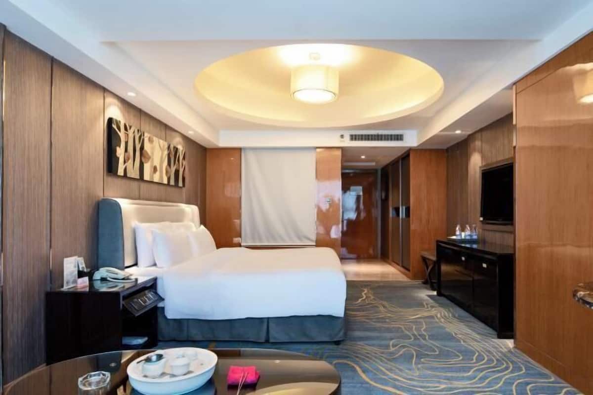 A hotel room with a bed, a desk, a TV, and a wall with artwork.