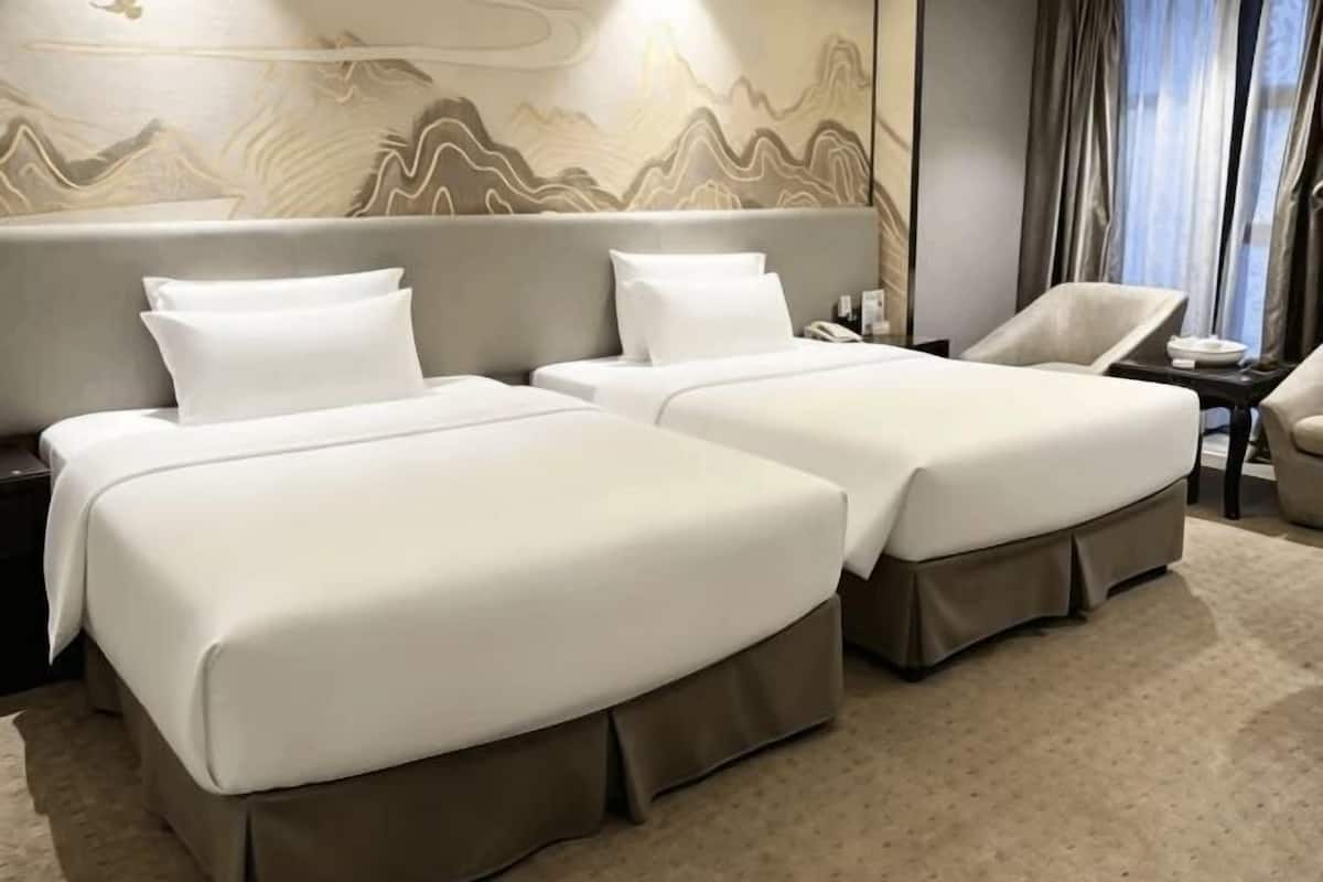 A hotel room with two beds, a chair, a nightstand, and a wall with a decorative pattern.