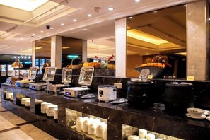 Een buffetopstelling met diverse food stations, waaronder een heetpot en een saladebar, in een goed verlichte ruimte.
