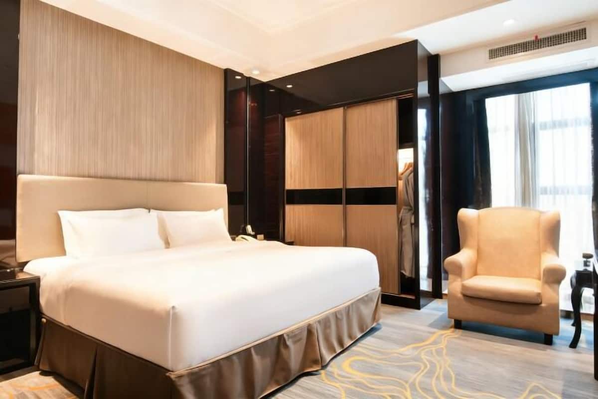 A hotel room with a large bed, a chair, a wardrobe, and a window.
