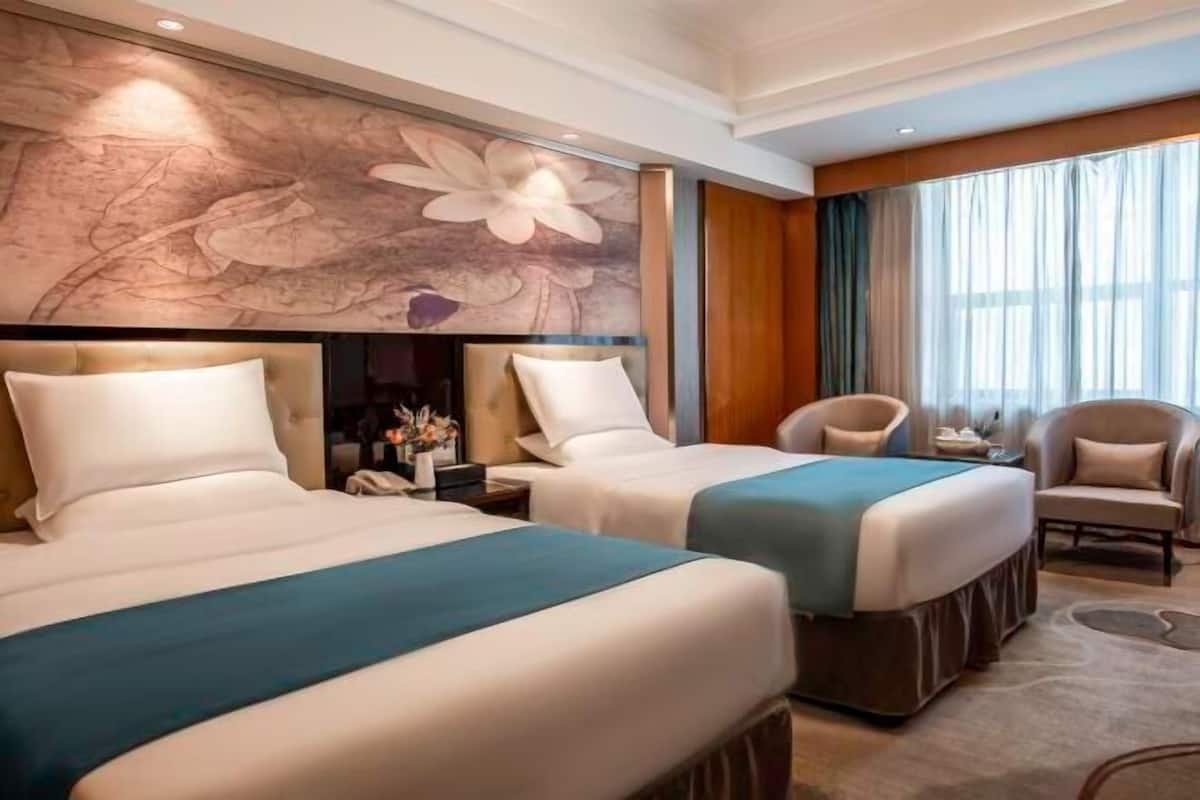 A hotel room with two beds, a large floral mural on the wall, a window with curtains, and a seating area with chairs.