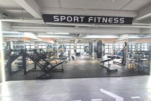 Un gimnasio con un letrero que dice 'SPORT FITNESS' y diverso equipamiento de ejercicio.
