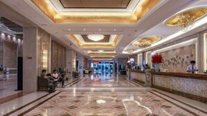 Un amplio vestíbulo de hotel con piso de mármol, una recepción y una lámpara de cristal.