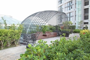 Une structure architecturale moderne, dotée d’un design en forme de dôme, entourée de verdure et comprenant un espace aménagé pour s’asseoir.