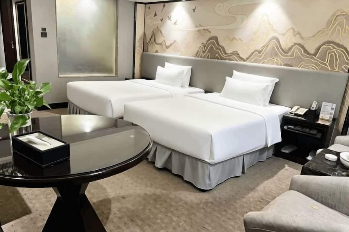 A hotel room with two beds, a round glass table, a nightstand, a chair, and a decorative wall.
