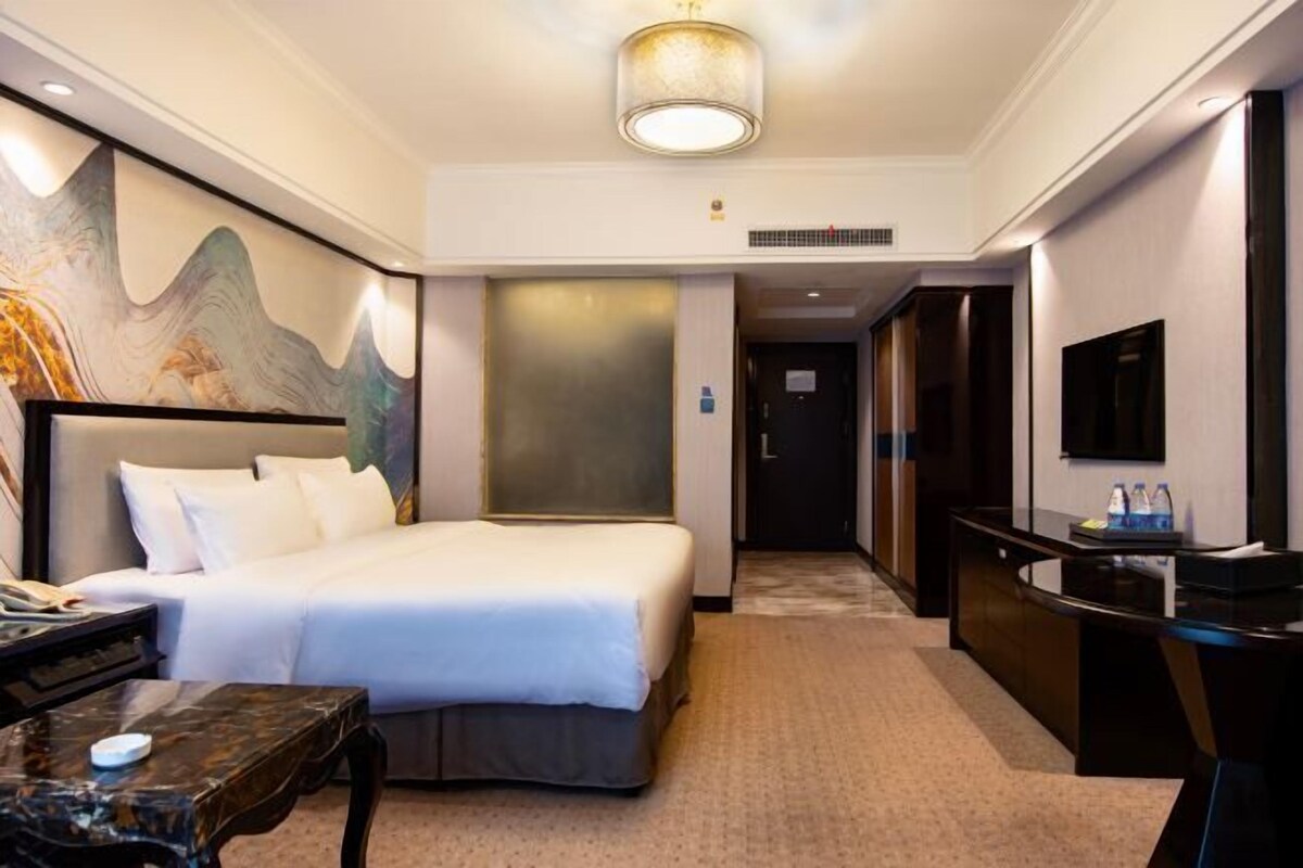 A hotel room with a bed, desk, and a large painting on the wall.
