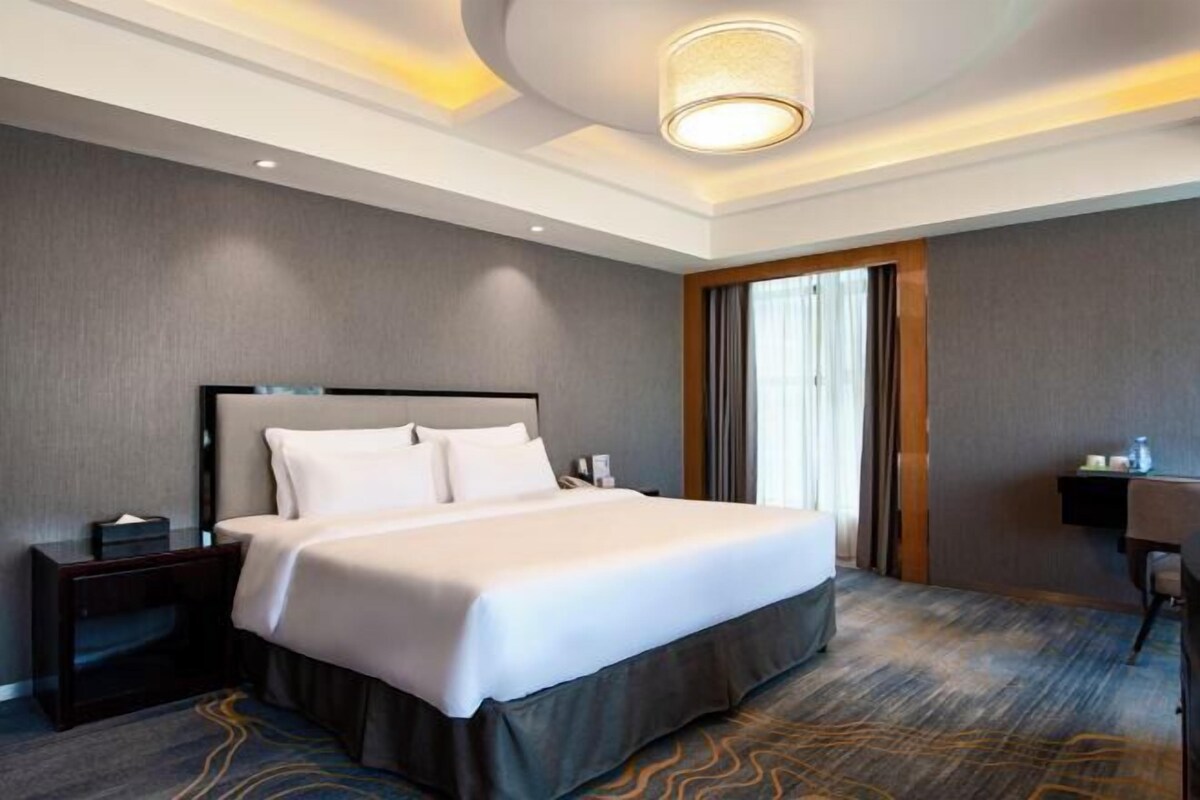 A hotel room with a large bed, a nightstand, a desk, and a window with curtains.