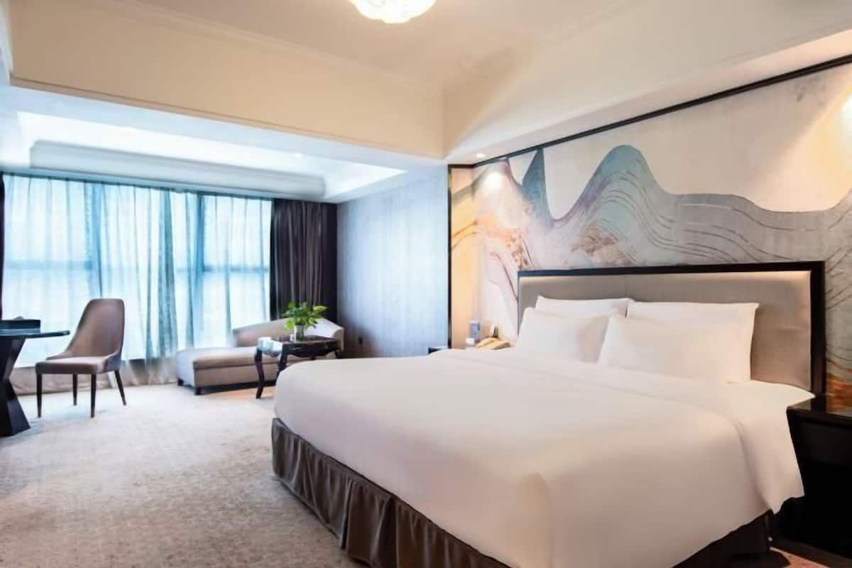 A hotel room with a large bed, a desk, a chair, and a view of the outdoors.