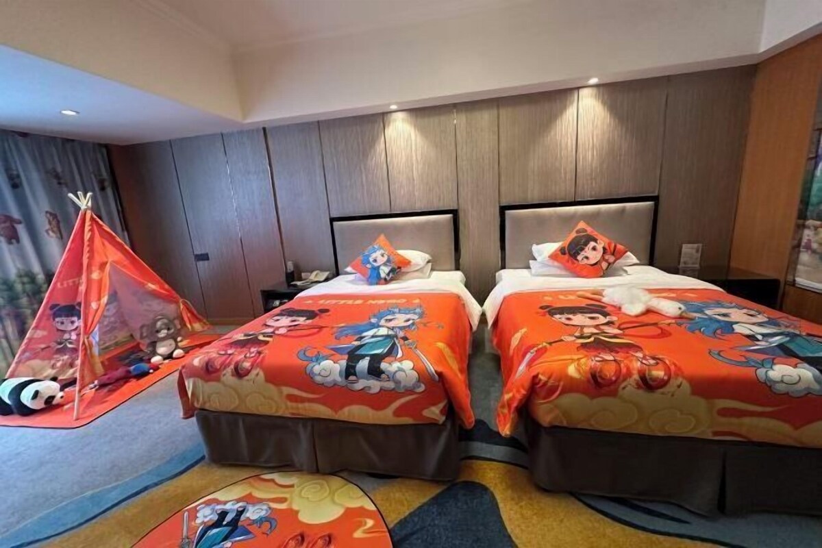 A hotel room with two beds, each with a cartoon-themed bedspread, a small play tent, and a plush toy on the floor.