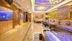 Un lobby de hotel lujoso con piso de mármol, un amplio conjunto de sofás, un televisor y un candelabro.