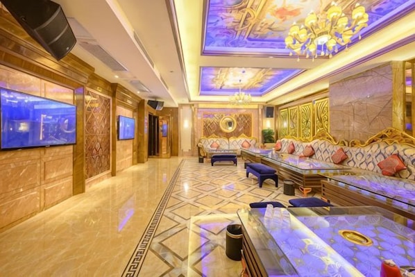 Un hall d’hôtel luxueux, avec un sol en marbre, un grand ensemble de canapés, un téléviseur et un lustre.