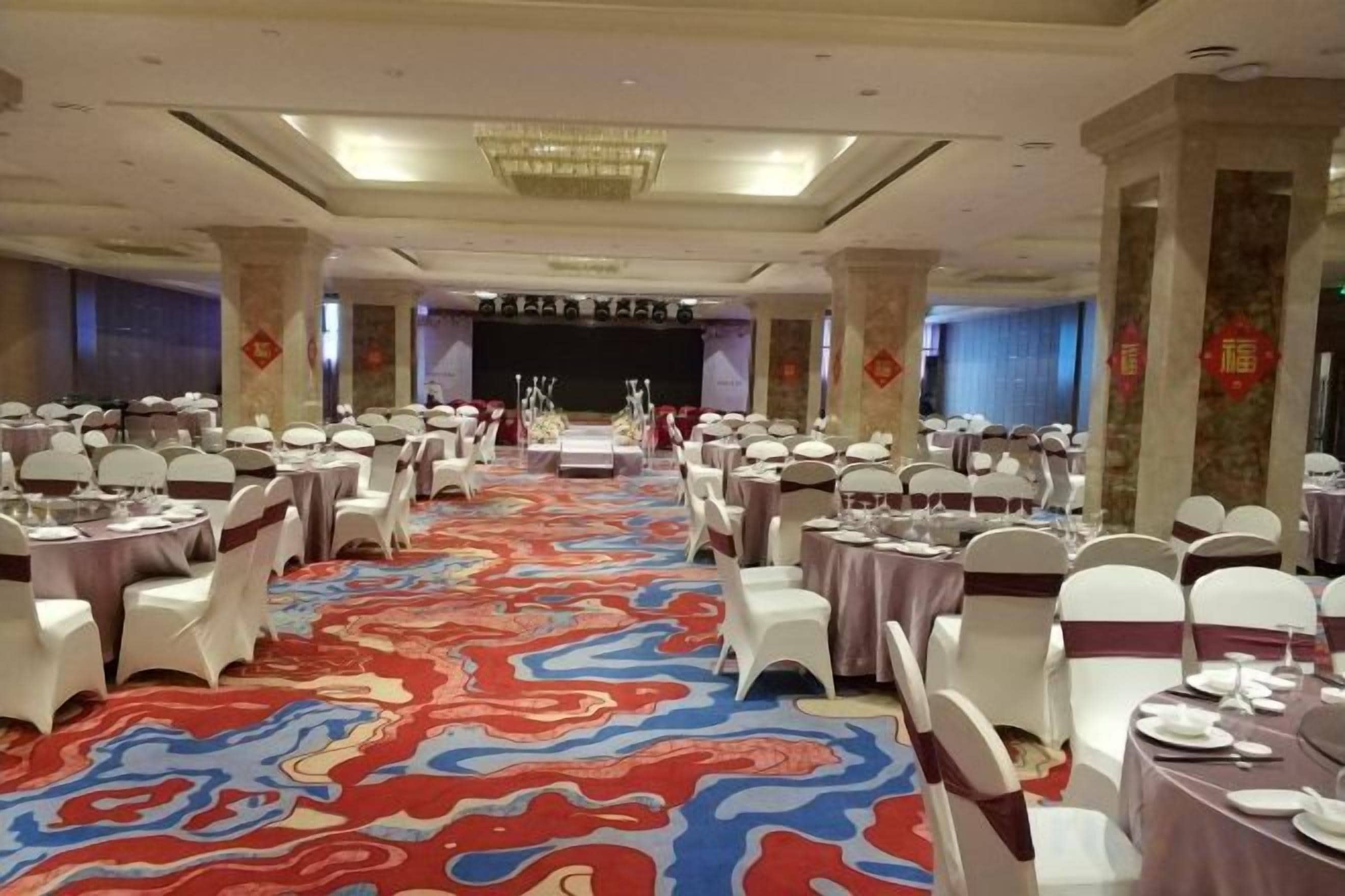 A banquet hall with round tables, white chairs, and a stage at the front.