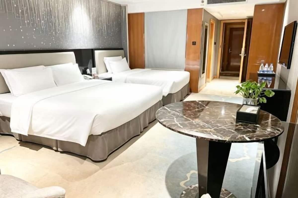 A hotel room with two beds, a marble table, a plant, and a minibar.