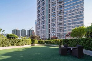 A rooftop terrace with a view of high-rise buildings, a well-maintained lawn, and outdoor furniture. - Shishi Wanjia International Hotel (Shishi)