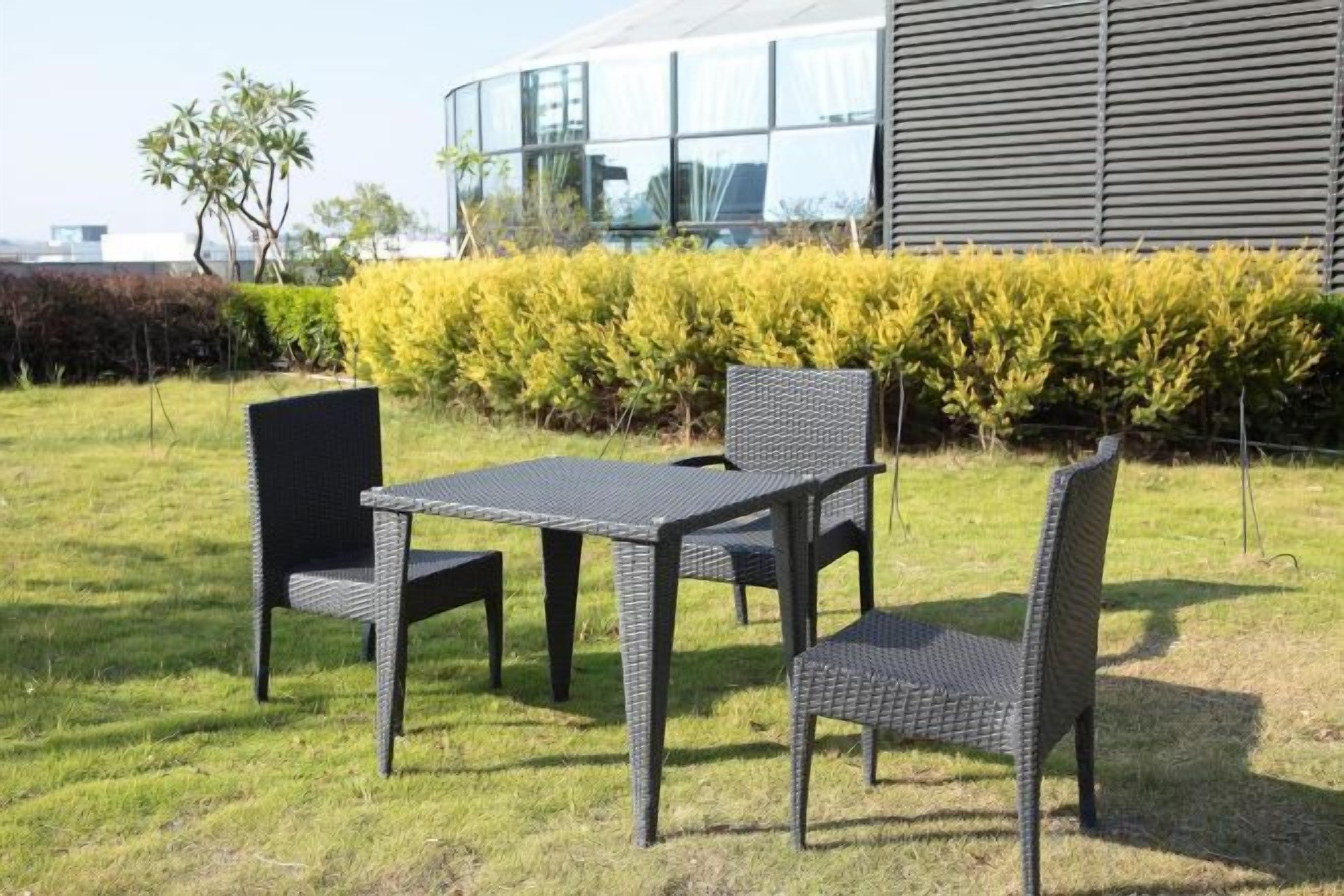 Un área de estar al aire libre con una mesa y sillas, un seto y un edificio moderno al fondo.