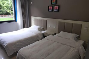 Une chambre d’hôtel avec deux lits, une fenêtre avec des rideaux et une vue sur la verdure.