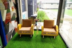 Two chairs with 'OIL BARREL' text, a small table with a vase, and a view of a courtyard through a glass door. - Beijing Slow Mountain Villa (Beijing)