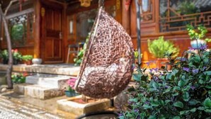 A traditional wooden building with a hanging woven structure, stone steps, and potted plants. - Lijiang Aduke Inn (Lijiang Ancient City Mufu Branch) (Lijiang)