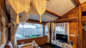 A wooden interior with a TV, a table with a pitcher and glasses, and a window with a view of traditional buildings. - Lijiang Aduke Inn (Lijiang Ancient City Mufu Branch) (Lijiang)