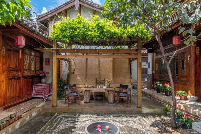 Um pátio tradicional com pérgola de madeira, mesa de jantar, cadeiras e plantas em vasos.
